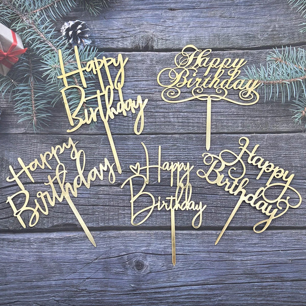 A set of elegant black and gold acrylic cake toppers with birthday messages on a weathered wooden background.