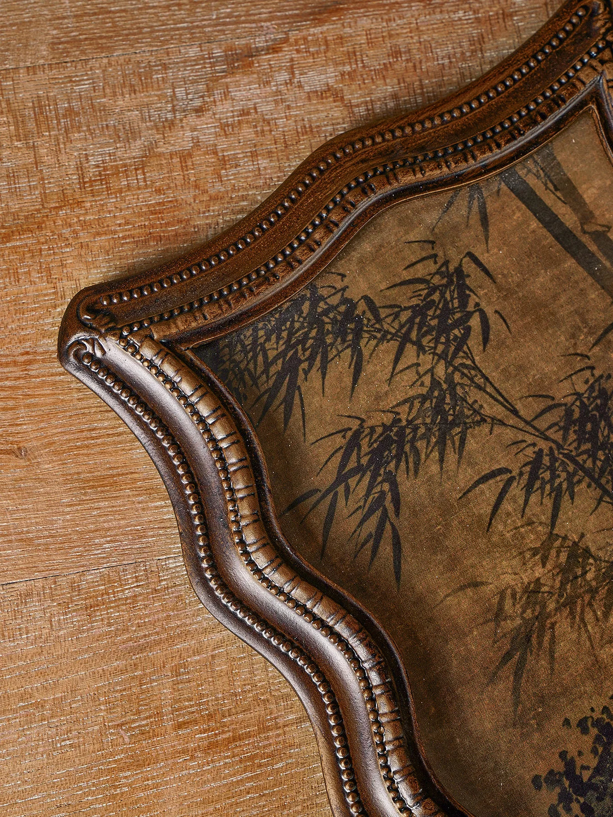 A vintage resin photo frame with a dark brown, distressed finish and a decorative, scalloped edge, set on a wooden surface.
