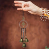 A hand holds a decorative witch bell wind chime with multiple small brass bells and a silver hoop.