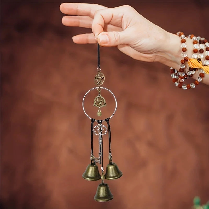 A hand holds a decorative witch bell wind chime with multiple small brass bells and a silver hoop.