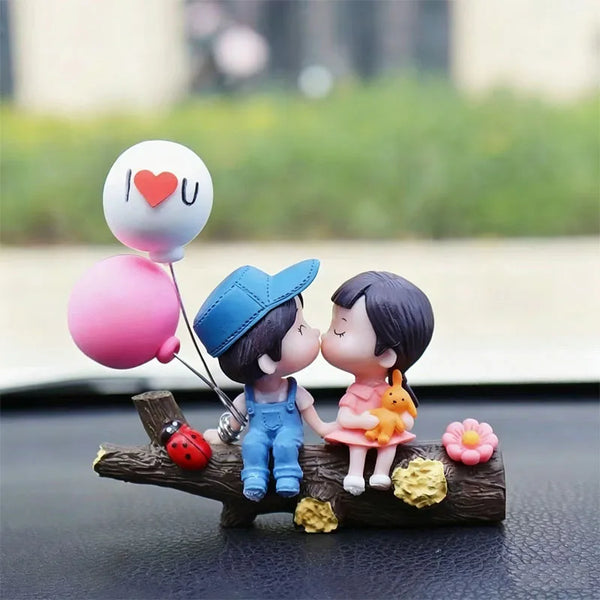 A cute couple figurine with a heart balloon, pink and blue, sitting on a wooden branch.