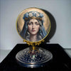 A golden framed religious medallion featuring a serene female face with blue hair and crown.