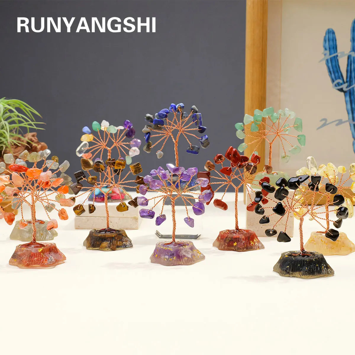 A display of seven crystal trees, each featuring natural stones in various colors like orange, purple, and green.