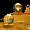 A golden crystal ball night light rests on a wooden base, illuminating sparkling light patterns against a dark background.