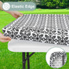 Black and white patterned elastic edge tablecloth being placed on a white table outdoors.