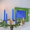 A set of blue stick candles displayed in a green box with decorative pinecone-shaped accents.