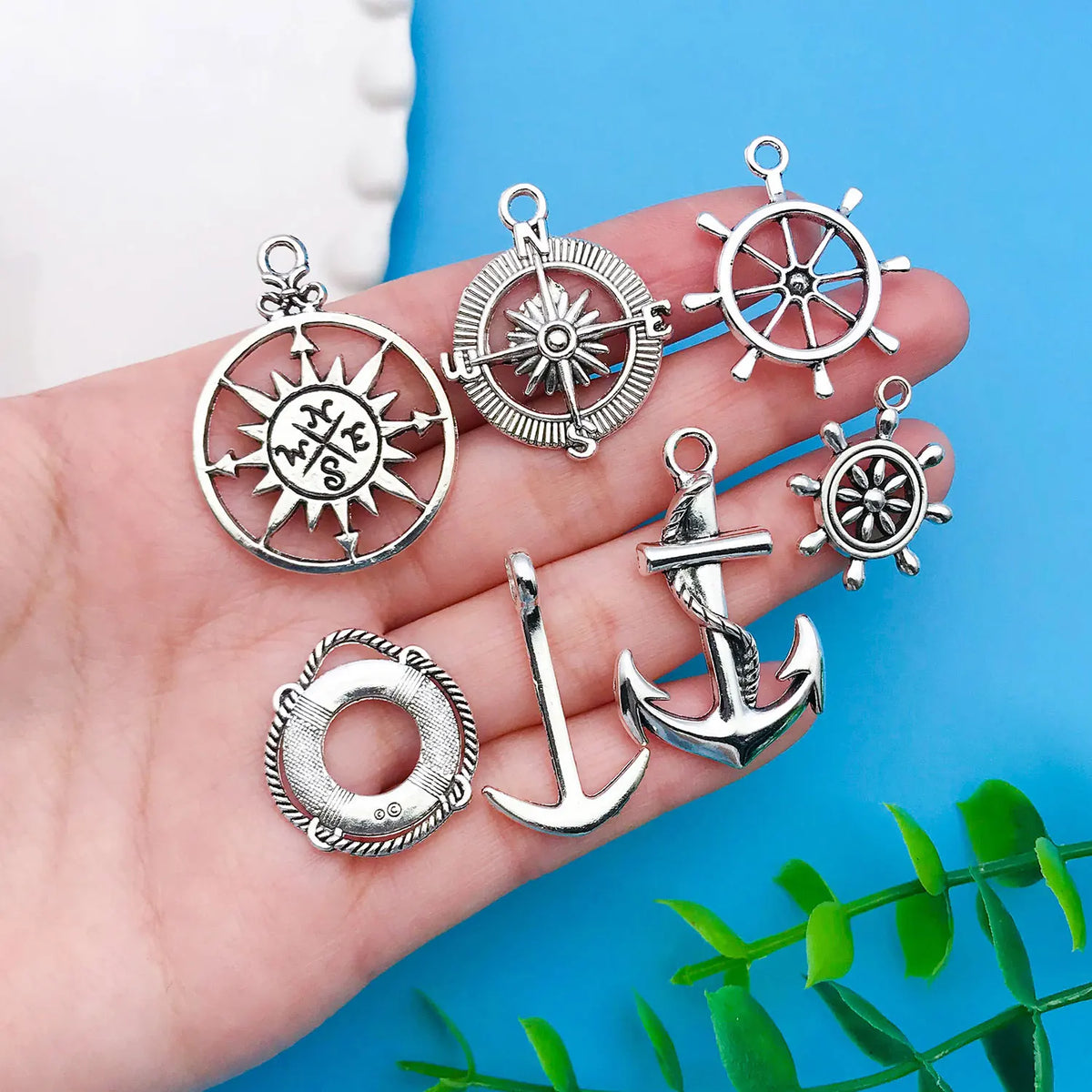 A hand holds various vintage ship anchor charms and medallions for jewelry making