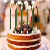 A round cake decorated with white frosting and fruit, surrounded by tall green candles.