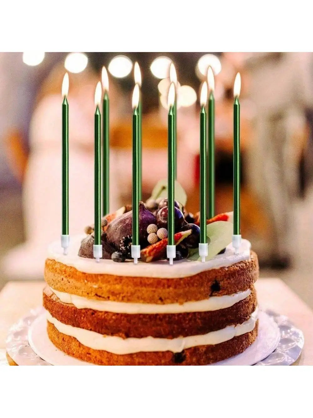 A round cake decorated with white frosting and topped with edible flowers and tall green birthday candles.