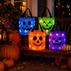 A glowing pumpkin candy bucket with LED handles sits on a wooden bench surrounded by autumn leaves and pumpkins.