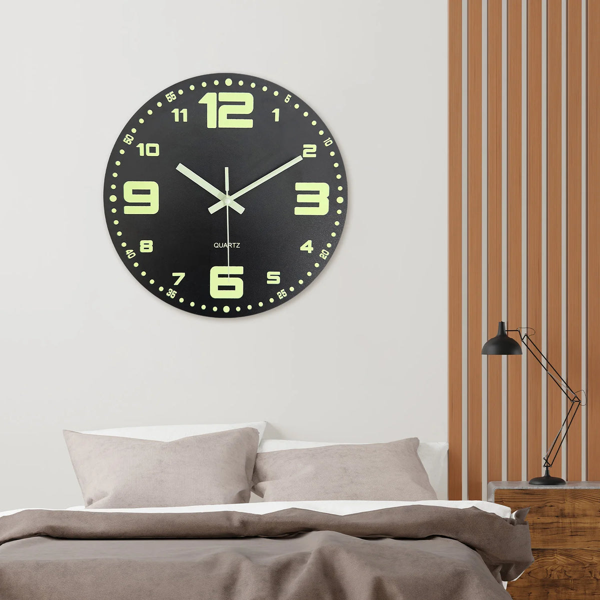 A round, black wall clock with a light green face and black numbers, mounted on a white wall next to vertical wooden slats.