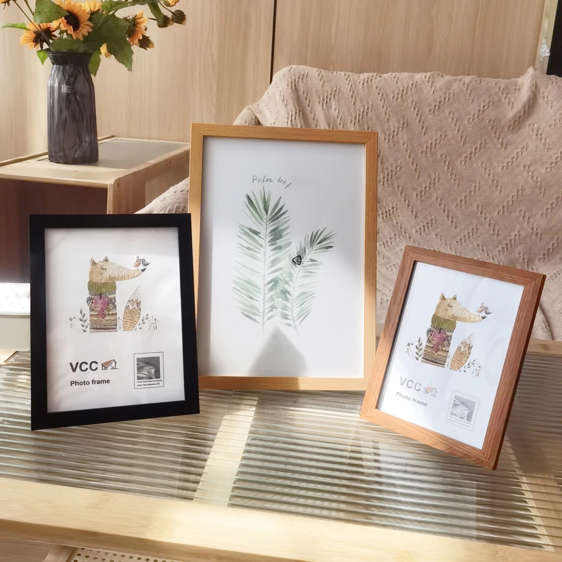 A set of five rustic wooden photo frames displayed on a light wooden table with greenery and soft textiles in the background.