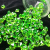 A pile of bright green crystal ice cube acrylic stones scattered on a dark surface.