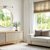 A modern living room features a large round vanity mirror with a matte metal frame above a wooden cabinet and a light-colored