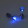 A close-up of a pair of blue LED light-up stud earrings resting on a surface.