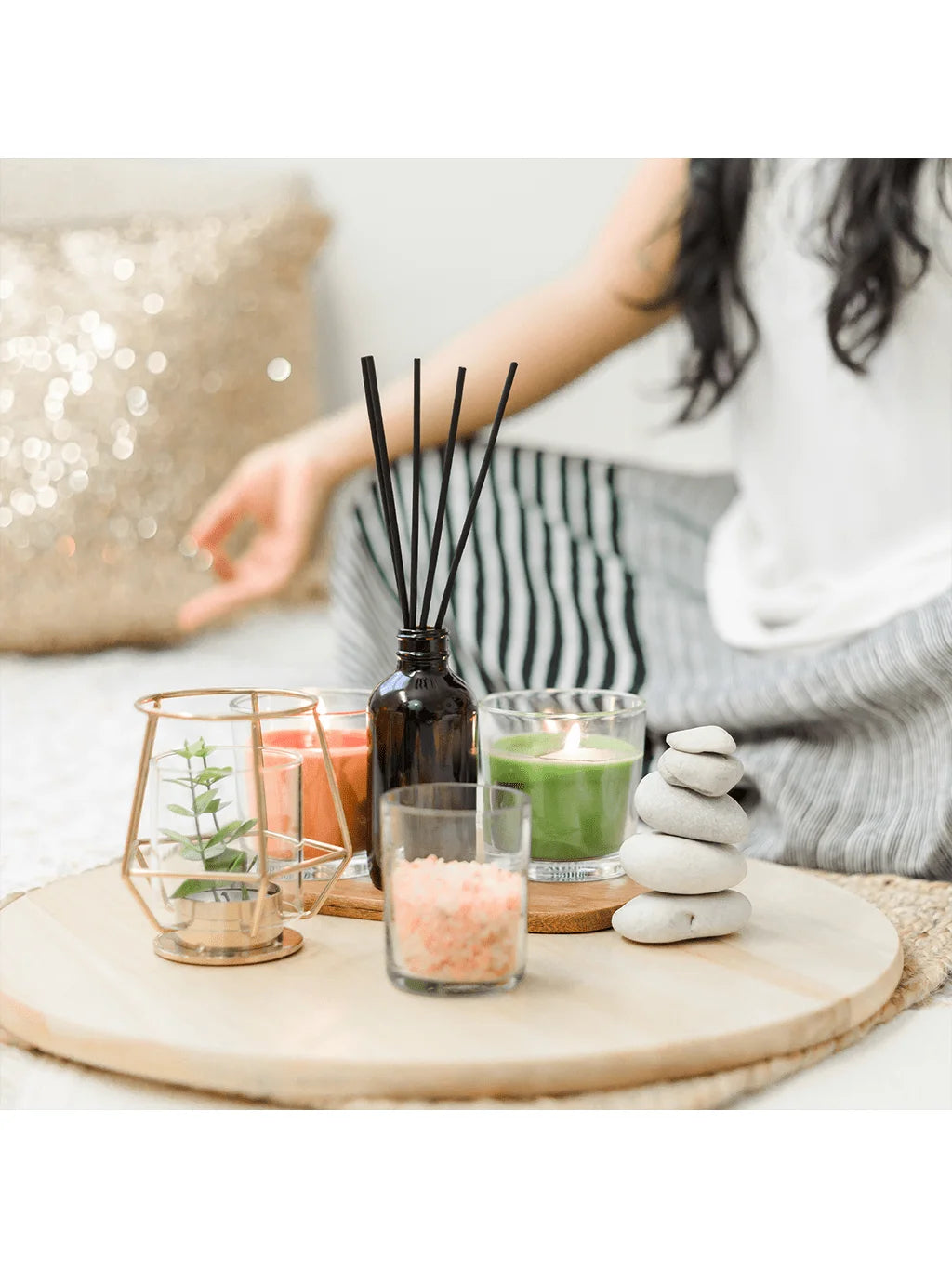 A hand holds a glass jar filled with black reeds and various colored wax dye blocks on a wooden surface.