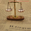 A vintage miniature balance scale with brass arms and wooden base is shown on a piece of paper.