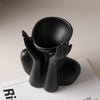 A black ceramic figural vase shaped like an artistic human form sitting on a white surface.