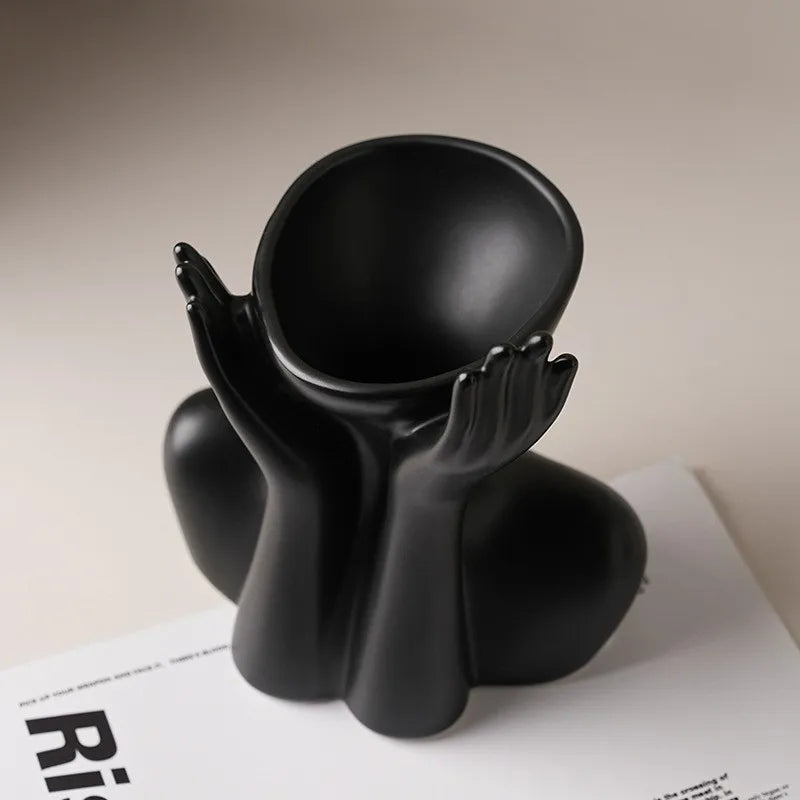 A black ceramic figural vase shaped like an artistic human form sitting on a white surface.