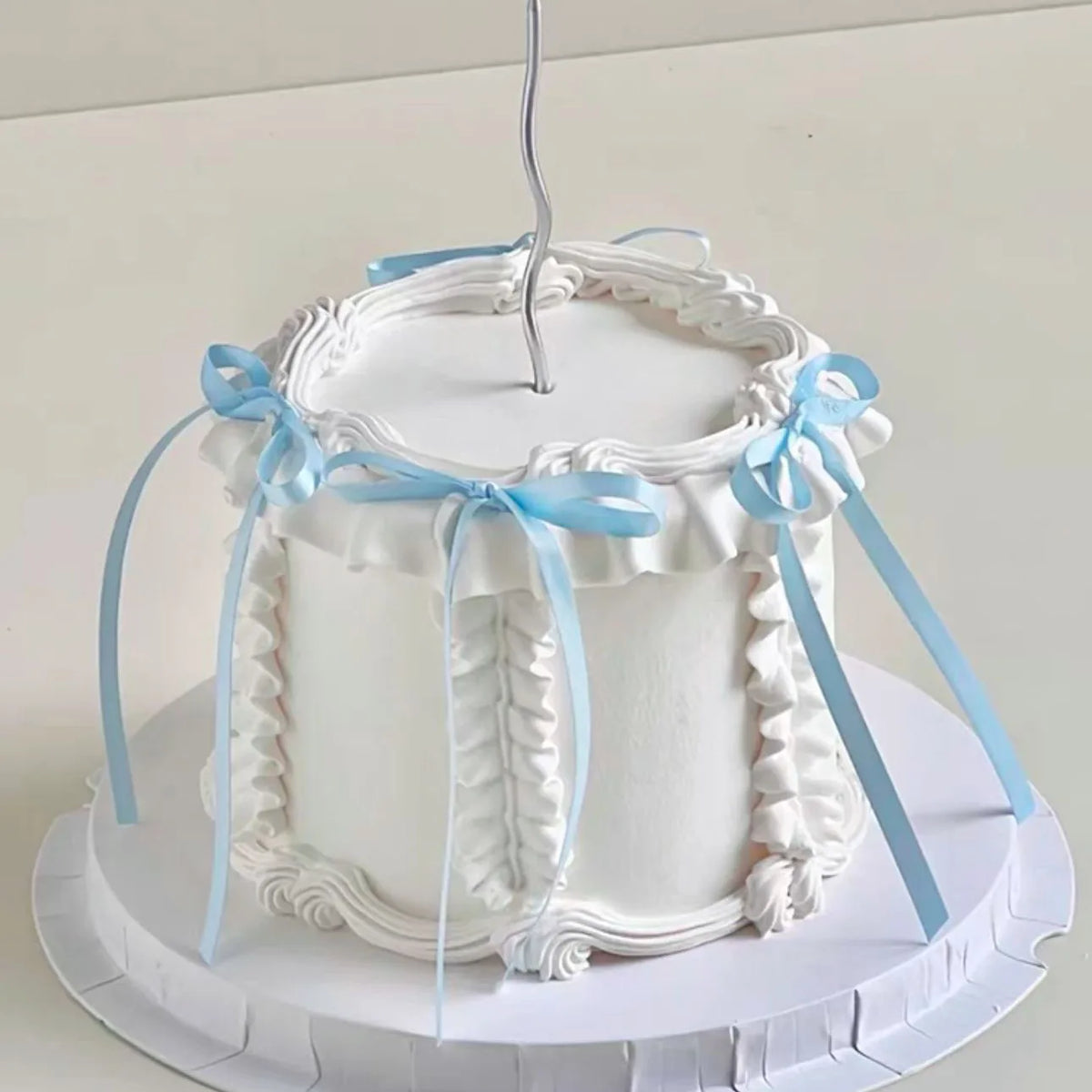A white cake decorated with ruffled borders and light blue ribbons, used as a birthday decoration.