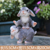 A gray resin rabbit garden statue with a pink nose sitting on a larger rabbit.