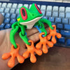 A green tree frog ornament with bright orange limbs is held over a blue keyboard.