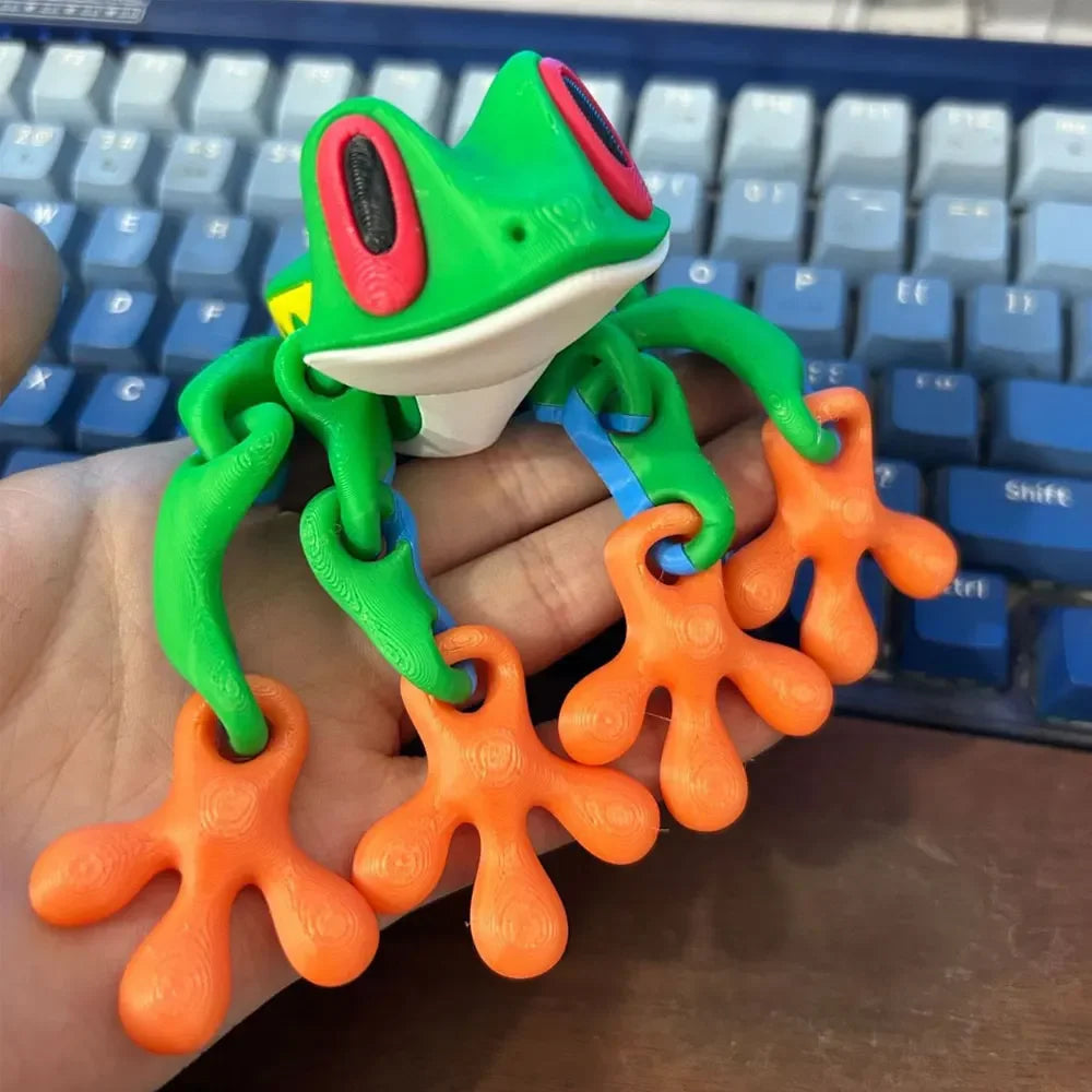 A green tree frog ornament with bright orange limbs is held over a blue keyboard.