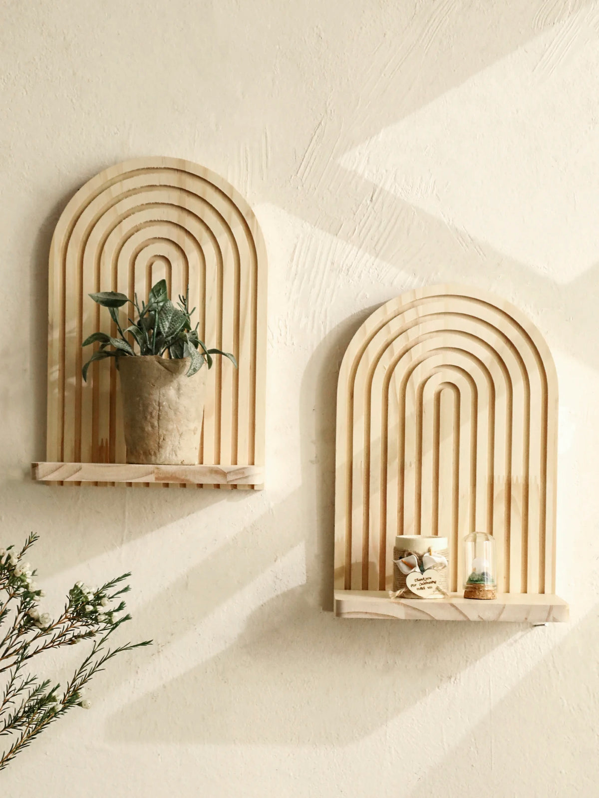 A set of geometric wooden wall shelves with arched grooves displaying a potted plant and a glass candle.