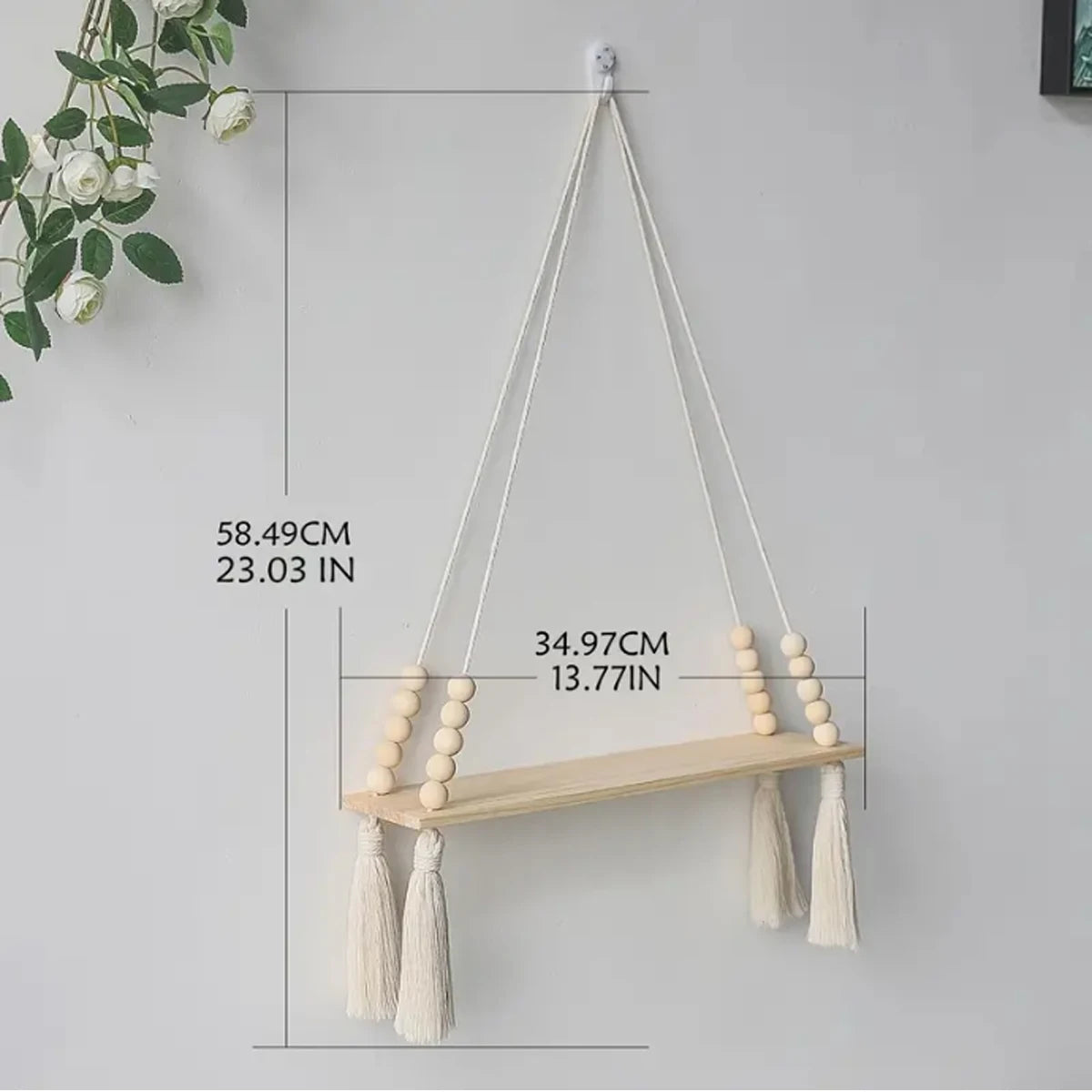 Handmade macrame wood wall shelf with tassels hanging on a white wall.