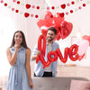 Junges Paar lächelt, umgeben von roten und rosa herzförmigen Ballons für einen romantischen Anlass.