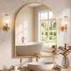 A bathroom featuring a white vessel sink and a large arched mirror with a gold frame above the counter.