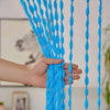 A hand is holding a bright blue beaded string curtain with tassels, showing the texture and drape of the bohemian decor.