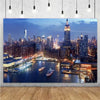 A photograph of the Night City skyline at dusk featuring illuminated high-rise buildings across a body of water.