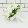 Elegant white silk rose bridal bouquet with green foliage tied with a white ribbon