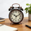 A vintage twin-bell alarm clock with a dark wooden casing and white face sits on a wooden table.