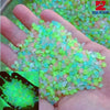 A hand holds a pile of glow-in-the-dark luminous green and pink pebbles.