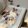 An open book displaying wooden comfort prayer crosses on a page, set on a light surface.