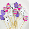 A collection of colorful, egg-shaped bamboo fruit skewers decorated with patterns and rabbit faces.