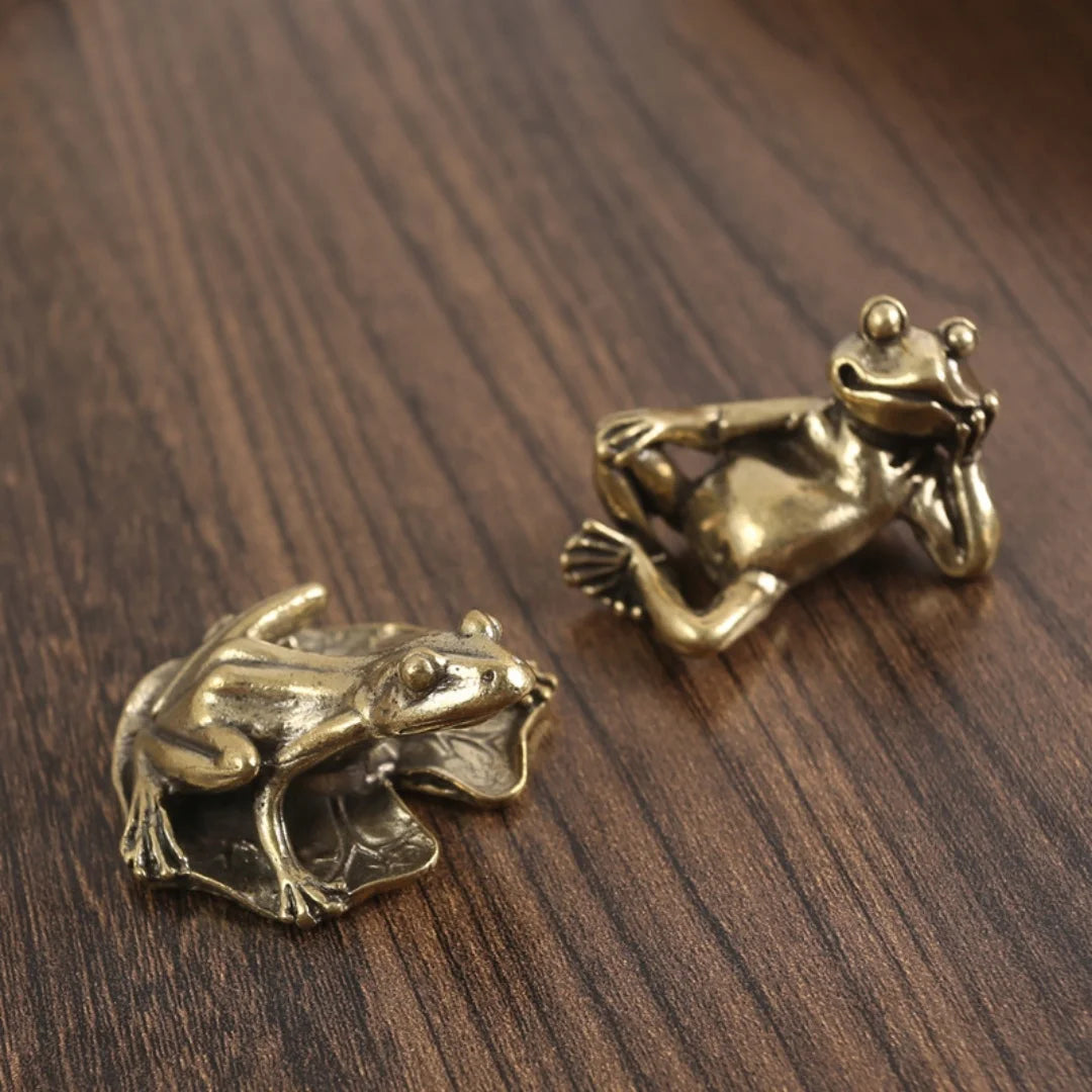 Antique brass frog sculpture decor resting on dark wood surface.