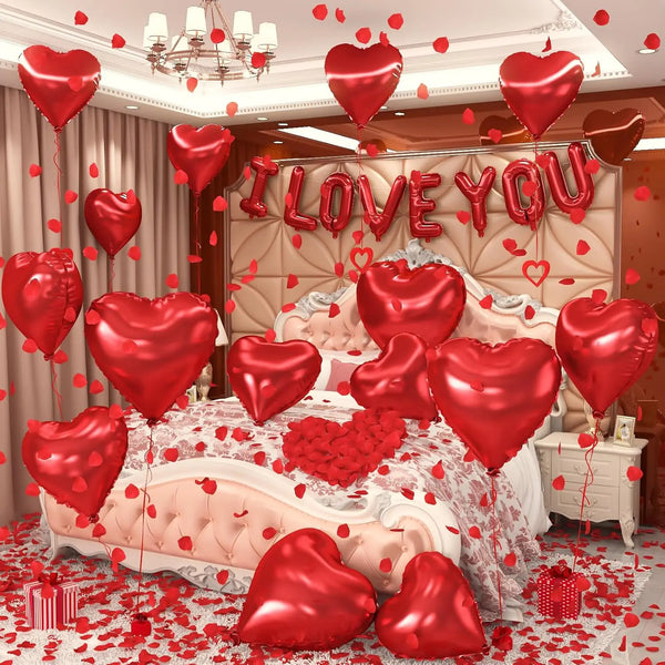 A display of red heart-shaped foil balloons and rose petals arranged around a pink bed for a romantic setting.