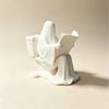 A white statue of a ghost reading a book sitting on a toilet.