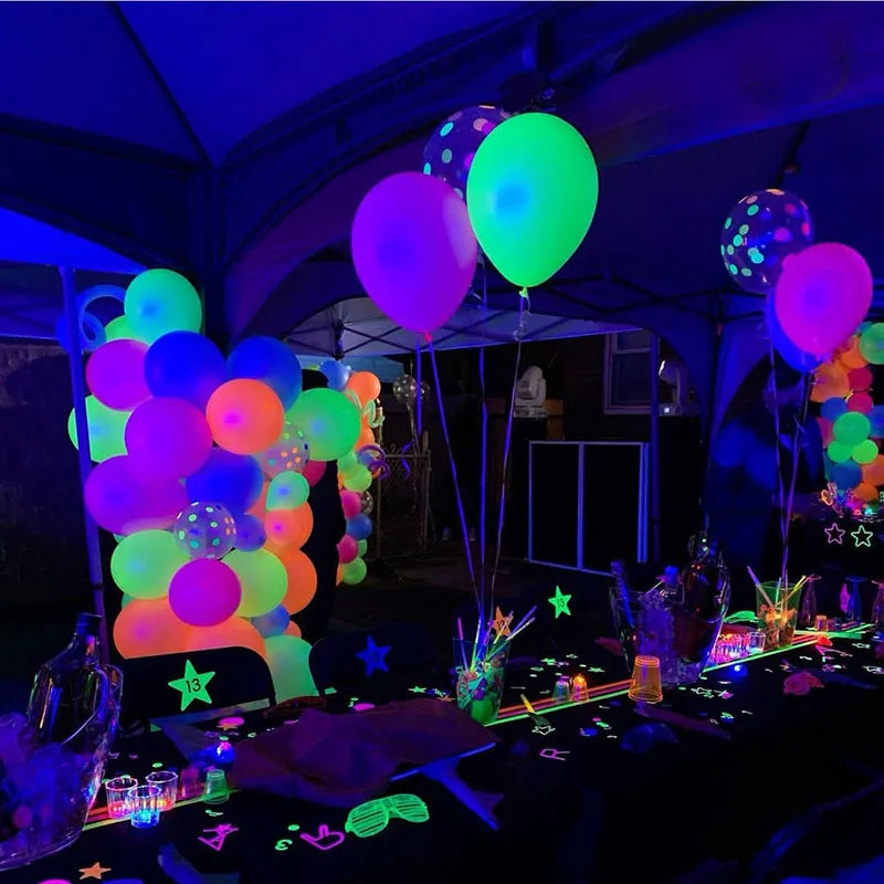 A dark party setting with neon glow-in-the-dark latex balloons in various colors like green, purple, and orange.