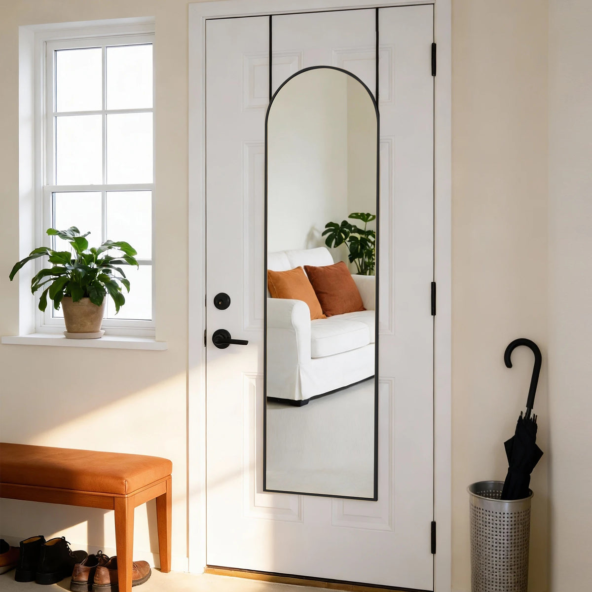 A full-length arched wall mirror with an aluminum frame is mounted on a white door, reflecting greenery and pillows.