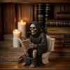 A dark resin statue of a hooded figure with a skull face holding a newspaper sitting on a wooden shelf.
