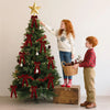 A young girl in a white sweater is decorating a Christmas tree with red velvet bows and ornaments.
