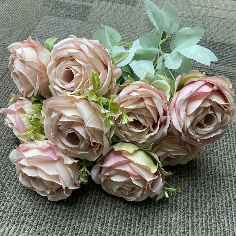 A bouquet of nine realistic silk roses in soft blush pink and cream tones with green foliage.