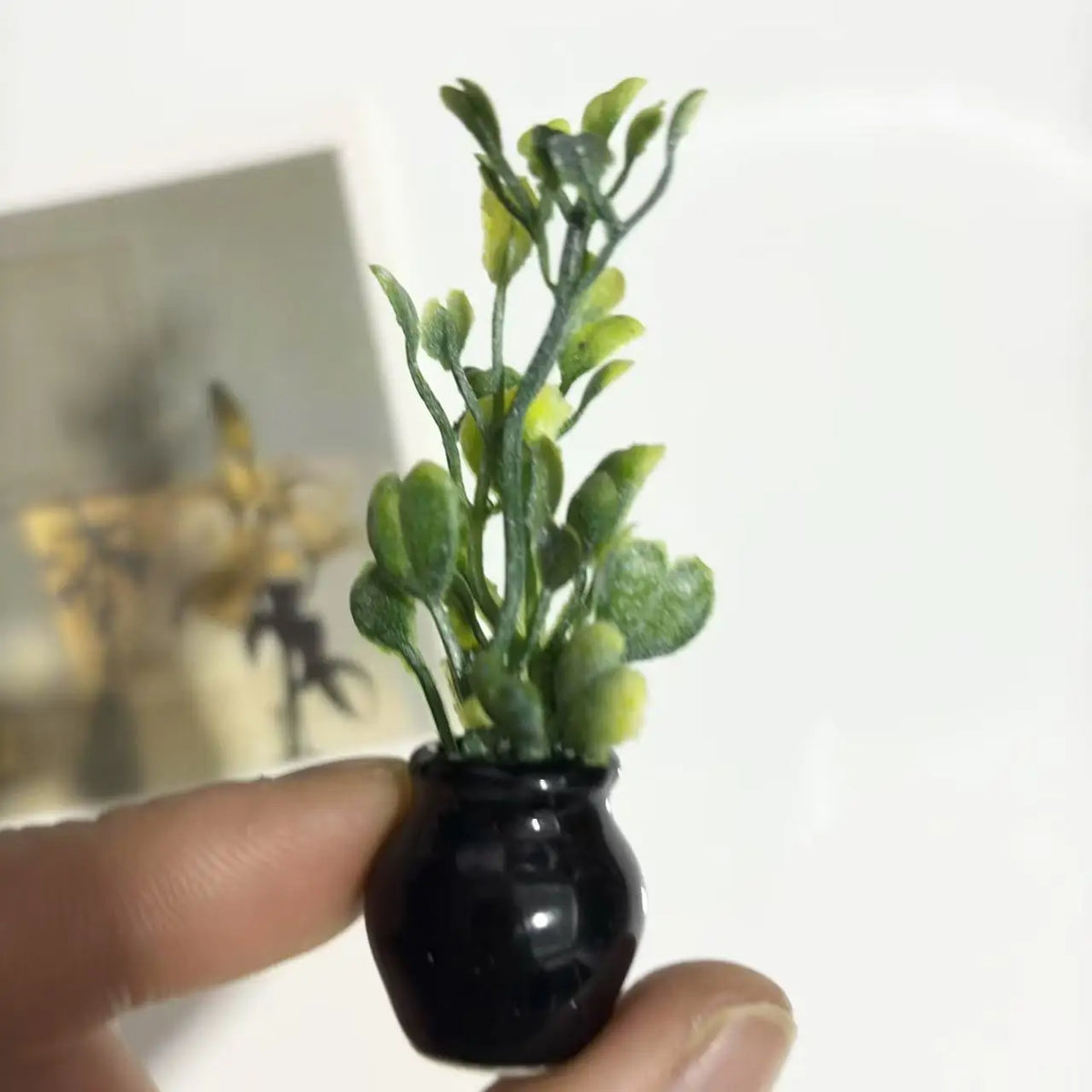 A small black ceramic vase holds a sprig of artificial green flowers.