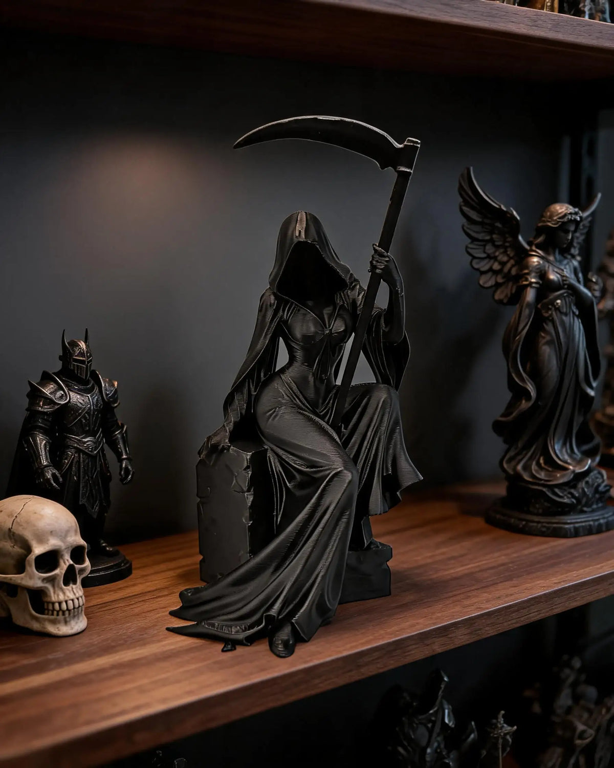A dark gothic female grim reaper figurine holding a scythe displayed on a wooden shelf.