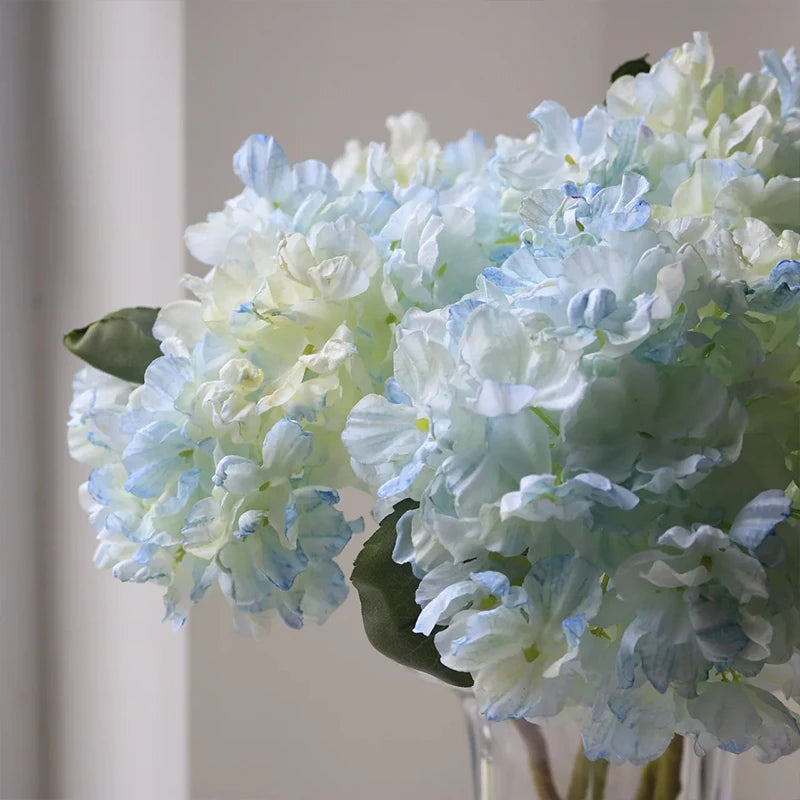 A close-up of a light blue silk hydrangea stem with vintage burnt edge petals in a clear vase.