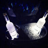 A close-up shot of two bottles illuminated by blue LED lights, resting on ice in a dark setting.